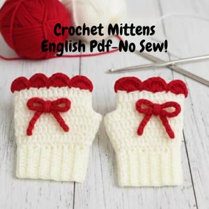 May include: A pair of white crochet mittens with red scalloped trim and a red bow. The mittens are displayed on a light wood surface. The text "Crochet Mittens English Pdf_No Sew!" is visible in the background.