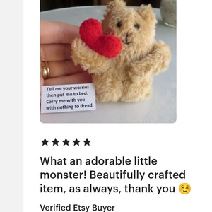 May include: A small, tan teddy bear holding a red heart. The bear has black eyes and a stitched nose. A small white card with text is visible. The text on the card reads: "Tell me your worries then put me to bed. Carry me with you with nothing to dread."