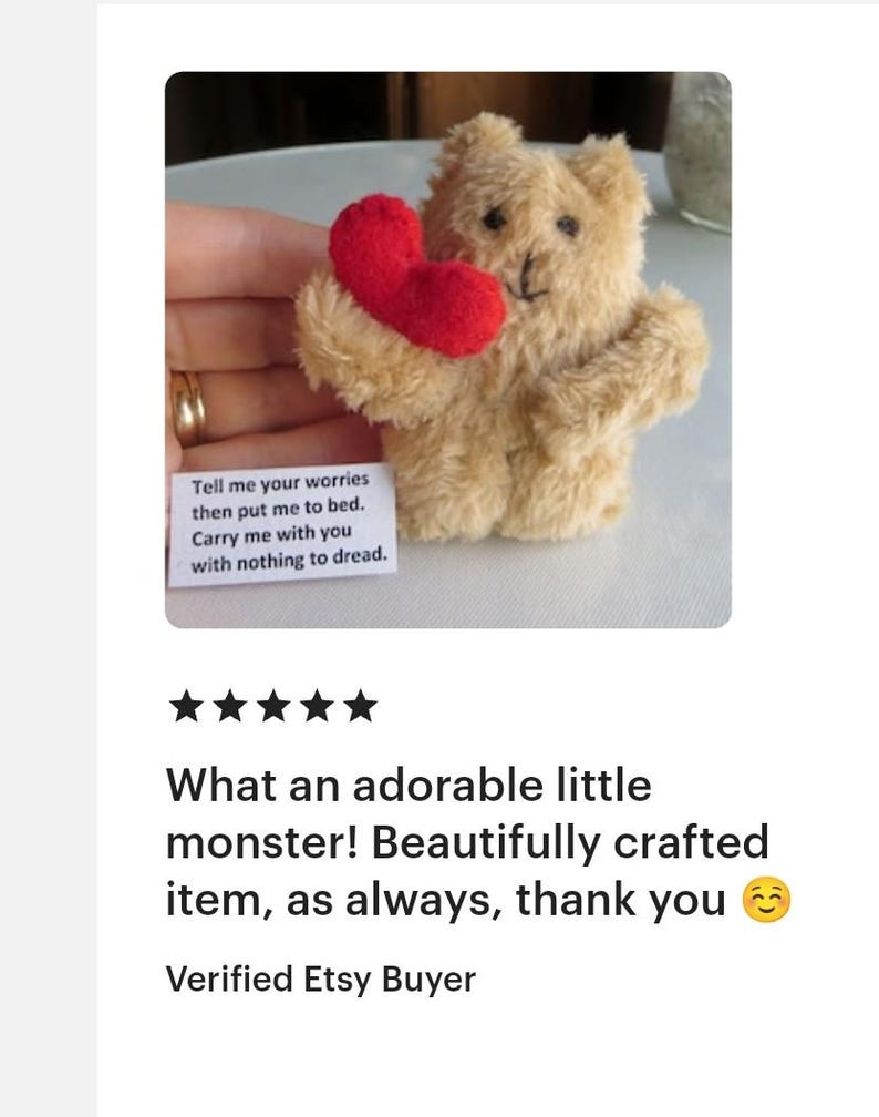 May include: A small, tan teddy bear holding a red heart. The bear has black eyes and a stitched nose. A small white card with text is visible. The text on the card reads: "Tell me your worries then put me to bed. Carry me with you with nothing to dread."