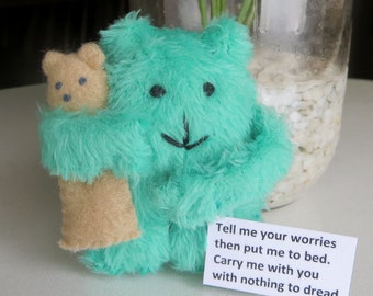 May include: A teal plush bear hugging a smaller tan bear. The bears have black stitched eyes and noses. A white card with black text reads, "Tell me your worries then put me to bed. Carry me with you with nothing to dread."