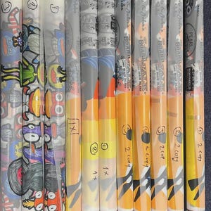 May include: A collection of eleven rolled paper menus or posters, some featuring colorful cartoon illustrations and others displaying the text 'Lenny & John's Boardwalk' and 'The Woo'. A black Sharpie marker is positioned horizontally below the rolls.