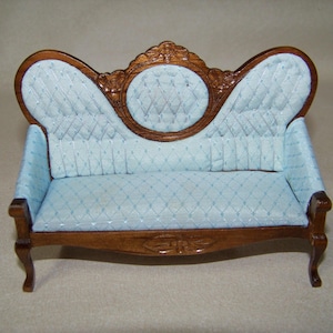 May include: Miniature antique-style sofa with a light blue quilted seat and back. The wooden frame is a dark brown with ornate carvings on the back and front apron. The sofa has curved arms and legs, and is designed for a dollhouse or similar setting.
