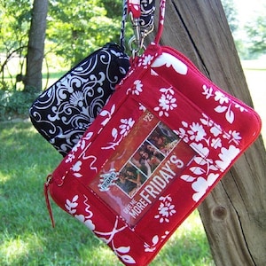 May include: A red and white patterned fabric wallet with a clear plastic window displaying a "Give Me More Fridays" gift card. The wallet has a black and white patterned fabric zipper pull and a black and white patterned fabric strap.