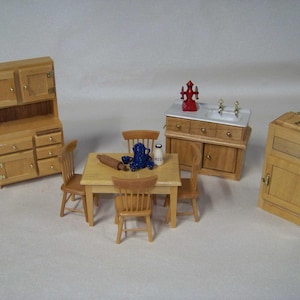 May include: Miniature wooden kitchen furniture set. Includes a hutch, table with chairs, a sink cabinet, and a refrigerator. The table has a rolling pin, a blue pitcher, and a milk bottle. The sink cabinet has a red fire hydrant decoration.
