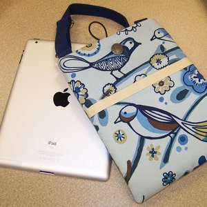May include: A blue and white fabric iPad case with a floral and bird design. The case has a strap and a flap closure. The text "iPad" is visible on the silver iPad.