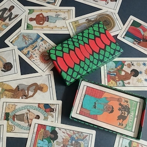 May include: A tarot card deck with colourful illustrations, scattered around an open and closed box. The boxes have a green and red pattern. The cards feature figures and symbols.