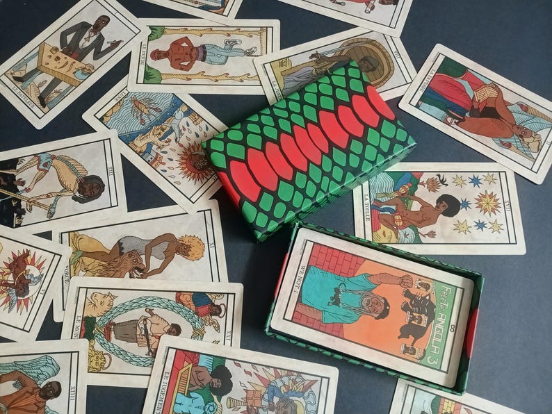 May include: A tarot card deck with colourful illustrations, scattered around an open and closed box. The boxes have a green and red pattern. The cards feature figures and symbols.