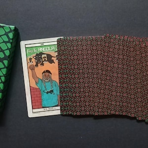 May include: A wallet with a brown and red geometric pattern, a card with an illustration of a person, and a wrapped item with a green and red snake skin pattern. The card has the text "Fist Angola" and "We Not I".
