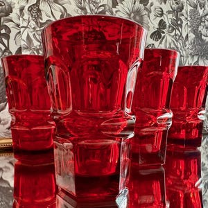 May include: Four red glass tumblers with a textured, faceted design. The glasses are arranged in a row, with the front glass in focus.