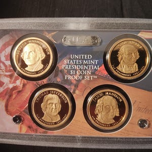 May include: A United States Mint Presidential $1 Coin Proof Set in a clear plastic case. The set includes five gold-colored coins featuring the portraits of George Washington, John Adams, Thomas Jefferson, James Madison, and James Monroe. The coins are arranged in a circle around the words "United States Mint Presidential $1 Coin Proof Set."
