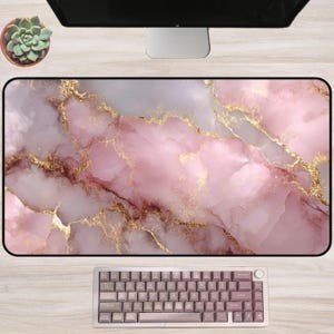 May include: A rectangular desk mat with a pink marble design and gold veining. A keyboard with pink keycaps sits on the mat. A small succulent in a brown pot is in the upper left corner.