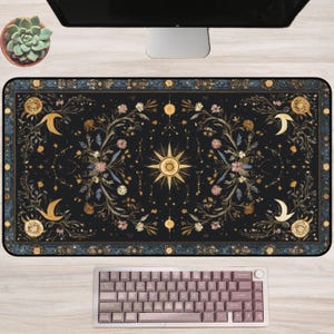 Puede incluir: Alfombrilla de escritorio rectangular negra con un diseño celestial que presenta un sol dorado, lunas crecientes y elementos florales. La alfombrilla tiene un borde azul oscuro y se combina con un teclado malva.