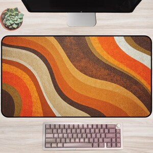 May include: A rectangular desk mat with a retro wavy pattern in shades of orange, brown, and beige. A computer keyboard is at the bottom, and a succulent in a pot is at the top left. The mat is designed for use with a computer.
