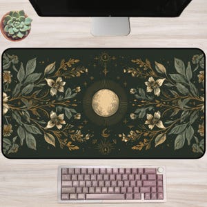 May include: A dark green desk mat featuring a celestial design with a central moon illustration, surrounded by floral and botanical elements in gold and white. A mauve keyboard is at the bottom.