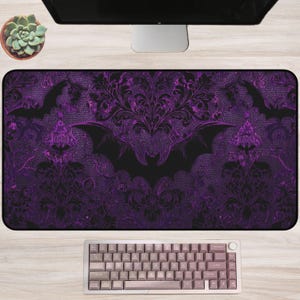 Può includere: Un tappetino da scrivania rettangolare con un design a pipistrello viola e nero. Il tappetino presenta un motivo floreale ripetuto e sagome di pipistrelli. Sono visibili una tastiera e un monitor del computer.