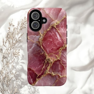 May include: A pink and gold phone case with a gemstone design. The case features a marbled pattern of pink and rose hues, accented with gold-colored veins. The phone case has a dual-lens camera cutout and black side buttons.
