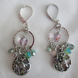 Puede incluir: Pendientes de plata con un dije de concha, cuentas de vidrio rosa y verde y un aro de plata.