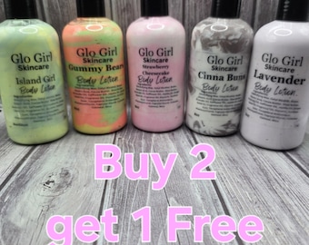 May include: Five bottles of Glo Girl Skincare body lotion in various scents: Island Girl, Gummy Bear, Strawberry Cheesecake, Cinna Buns, and Lavender. Each bottle has a black cap and a label with the product name. The text "Buy 2 get 1 Free" is displayed in pink.