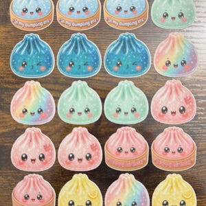 May include: A collection of twenty die-cut stickers featuring cartoon dumplings with expressive faces. Some dumplings are in bamboo steamers with text reading In my dumpling era or Happy birthday. Colors include blue, green, pink, yellow, and rainbow.
