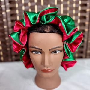 May include: A satin hair bonnet in green and red. The bonnet is designed with a ruffled edge, showcasing a vibrant contrast between the two colors. The bonnet is displayed on a mannequin head.