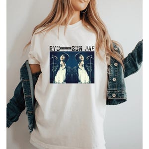 May include: White t-shirt with a black and white image of two men singing into microphones. The text "RYU - SUN JAE" is printed above the image.