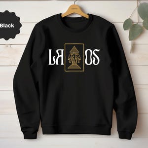 Könnte beinhalten: Schwarzer Pullover mit einem goldenen Design aus drei Elefanten und einem Tempel mit dem Wort "LAOS" in weißer Schrift.