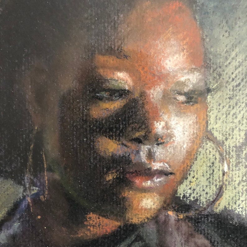 Op de afbeelding: Een close-up portret van een persoon met een donkere huid en donker haar. De persoon draagt grote oorringen en heeft een zachte, contemplatieve uitdrukking.
