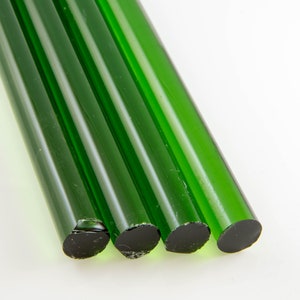 Könnte beinhalten: Vier grüne Glasstäbe mit schwarzen Enden. Die Stäbe sind in einer Reihe angeordnet, wobei die Enden der Stäbe zum Betrachter zeigen.