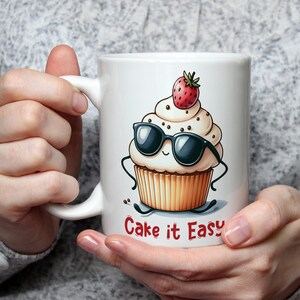 May include: White ceramic mug featuring a cartoon cupcake with sunglasses and a strawberry on top. The text "Cake it Easy" is printed on the mug.