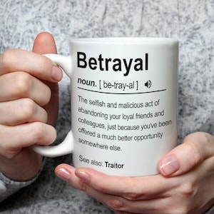 May include: White ceramic mug featuring the definition of "Betrayal" in black text. The definition includes pronunciation and a description of the act. The mug is held by a person.