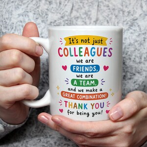 May include: A white ceramic mug featuring colorful text that reads: It's not just COLLEAGUES we are FRIENDS, we are A TEAM, and we make a GREAT COMBINATION! THANK YOU for being you! The design includes small red hearts and yellow star accents.