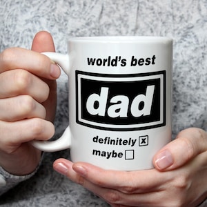 May include: A white ceramic mug featuring the black text world's best dad inside a rectangular border. Below the box, the text definitely is followed by an X in a square checkbox, and the word maybe is followed by an empty square checkbox.