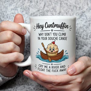 Puede incluir: Taza de cerámica blanca con el texto "Hey Cuntmuffin" y "Why don't you climb in your douche canoe". La taza presenta un cupcake de dibujos animados en una canoa y el texto "Cry me a river and float the fuck away".