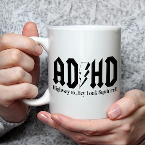 May include: White ceramic mug with a black and white graphic that says "ADHD Highway to...Hey Look Squirrel!"