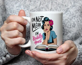 May include: White ceramic mug with a black and pink design. The mug features a cartoon woman with a pink flower in her hair and the text "I'm not mean I'm brutally honest".