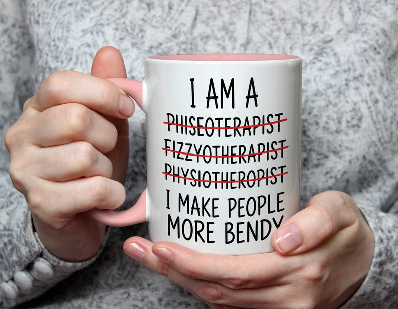 May include: White ceramic mug with a pink interior and handle. The mug has the text "I AM A... I MAKE PEOPLE MORE BENDY" with crossed-out words. The mug is held by a person.