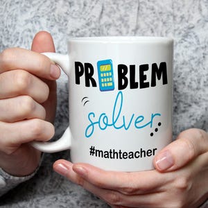 May include: White ceramic mug with the words "PROBLEM solver" in black and teal lettering, with a calculator graphic. The mug also includes the hashtag "#mathteacher".