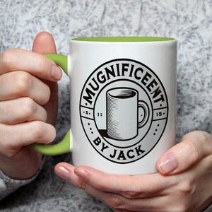 May include: White ceramic mug with a green handle and a black and white design that says "Mugnificent By Jack".