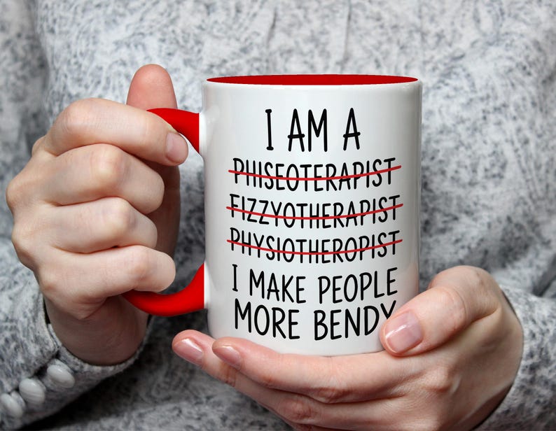 May include: White ceramic mug with a red interior and handle. The mug features the text "I AM A... I MAKE PEOPLE MORE BENDY" with crossed-out words. The mug is held by a person.