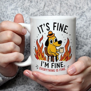 May include: White ceramic mug with a cartoon dog in a hat, sitting in a chair surrounded by flames, holding a coffee cup. The mug has the text "IT'S FINE. I'M FINE. EVERYTHING IS FINE."