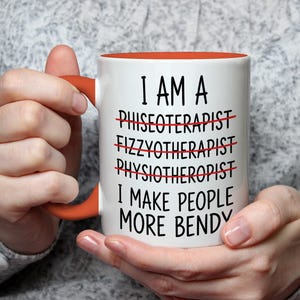 May include: White ceramic mug with an orange interior and handle. The mug features the text "I AM A... I MAKE PEOPLE MORE BENDY" with crossed-out words. The mug is held by a person.