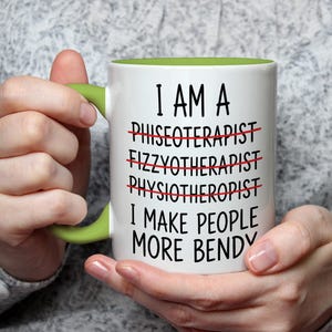 May include: White ceramic mug with a green handle and interior. The mug features the text "I AM A... I MAKE PEOPLE MORE BENDY" with crossed-out words. A humorous gift for a physical therapist.