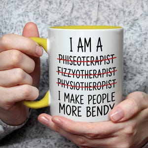May include: White ceramic mug with a yellow handle and interior. The mug features the text "I AM A... I MAKE PEOPLE MORE BENDY" with crossed-out words. The mug is held by a person.