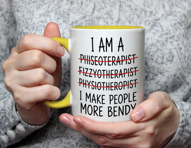 May include: White ceramic mug with a yellow handle and interior. The mug features the text "I AM A... I MAKE PEOPLE MORE BENDY" with crossed-out words. The mug is held by a person.