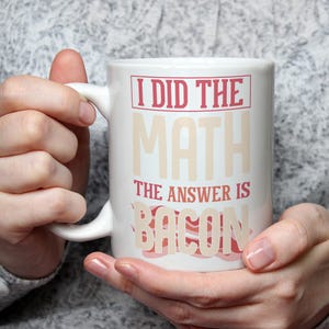 May include: White ceramic mug with a red and white design. The mug says "I did the math, the answer is bacon".