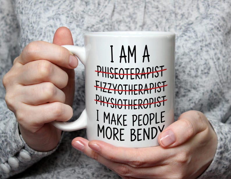 May include: White ceramic mug with black text that reads "I AM A... I MAKE PEOPLE MORE BENDY." The words "PHISEOTERAPIST," "FIZZYTHERAPIST," and "PHYSIOTHERAPIST" are crossed out in red. The mug is held by a person.