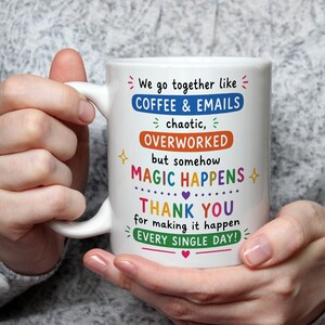 Pode incluir: Uma caneca de cerâmica branca com texto colorido que diz: We go together like COFFEE & EMAILS, chaotic, OVERWORKED, but somehow MAGIC HAPPENS, THANK YOU for making it happen EVERY SINGLE DAY! O design inclui pequenas estrelas, corações e traços.