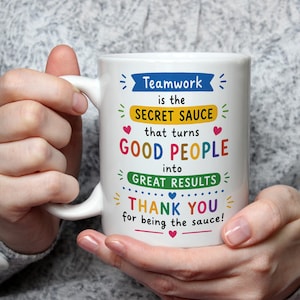 May include: A white ceramic mug featuring colourful text that reads: Teamwork is the SECRET SAUCE that turns GOOD PEOPLE into GREAT RESULTS THANK YOU for being the sauce! The design includes small pink and blue hearts and decorative lines.