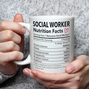 Könnte beinhalten: Weiße Keramik-Tasse mit dem Text "SOCIAL WORKER Nutrition Facts" und einem rosa Herz. Die Tasse listet Eigenschaften wie "Great Listener" und "Problem Solver" mit Prozentwerten auf. Die Tasse wird von einer Person gehalten.