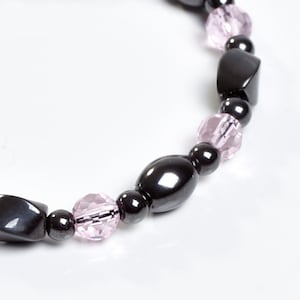 May include: A black and pink beaded bracelet with oval and rectangular shaped beads.